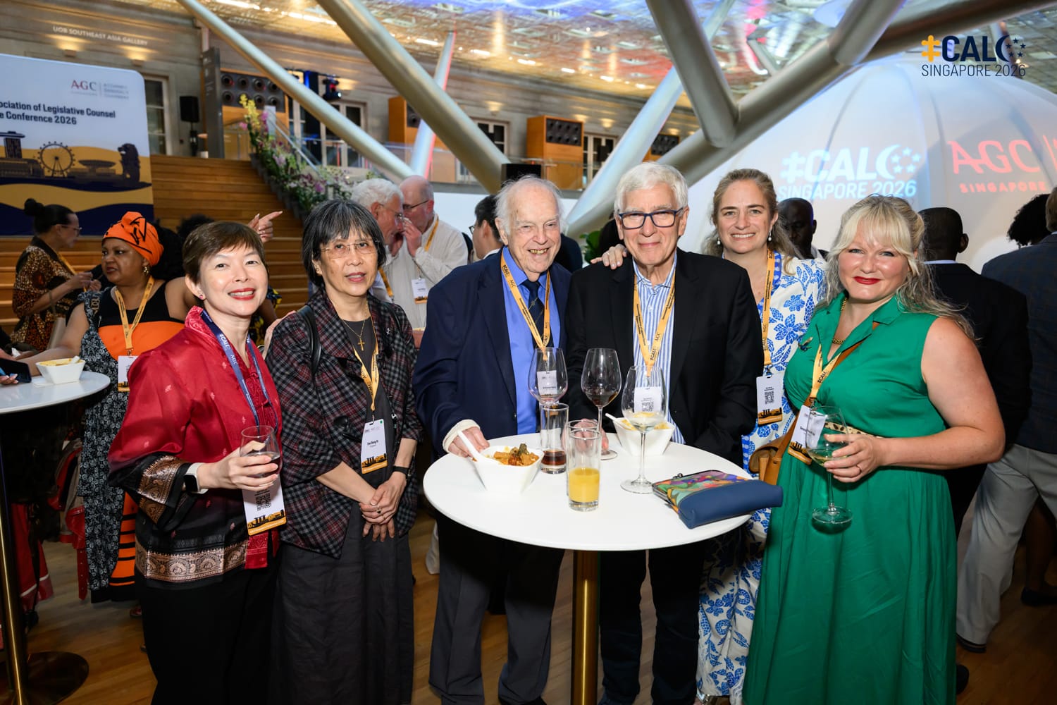 Six conference attendees, including Ms Jeanne Lee, Chief Legislative Counsel of Singapore, pose together at a networking reception for CALC Singapore 2026, with drinks and food on a high table, and the AGC Singapore branding visible in the background.